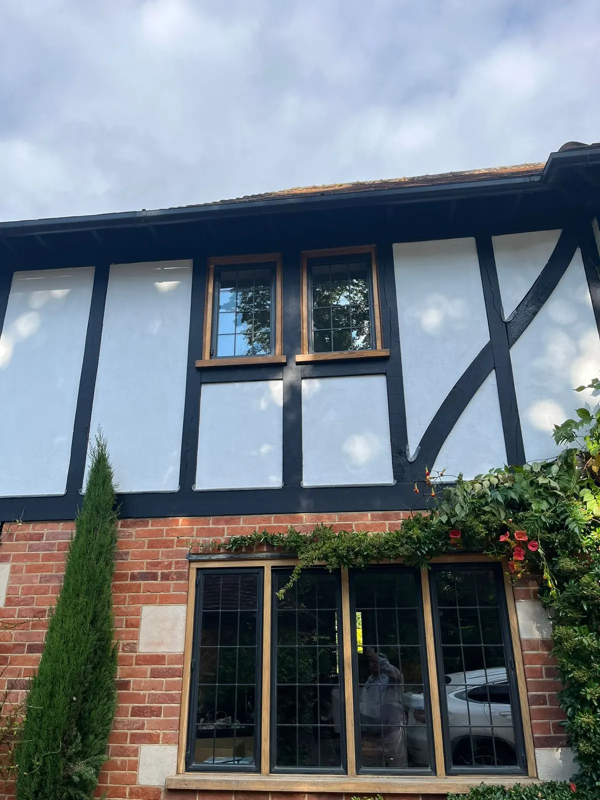 Freshly painted Tudor-style Surrey home exterior with black timber framing and white render panels above red brick, finished by Martin And Co. Decorating